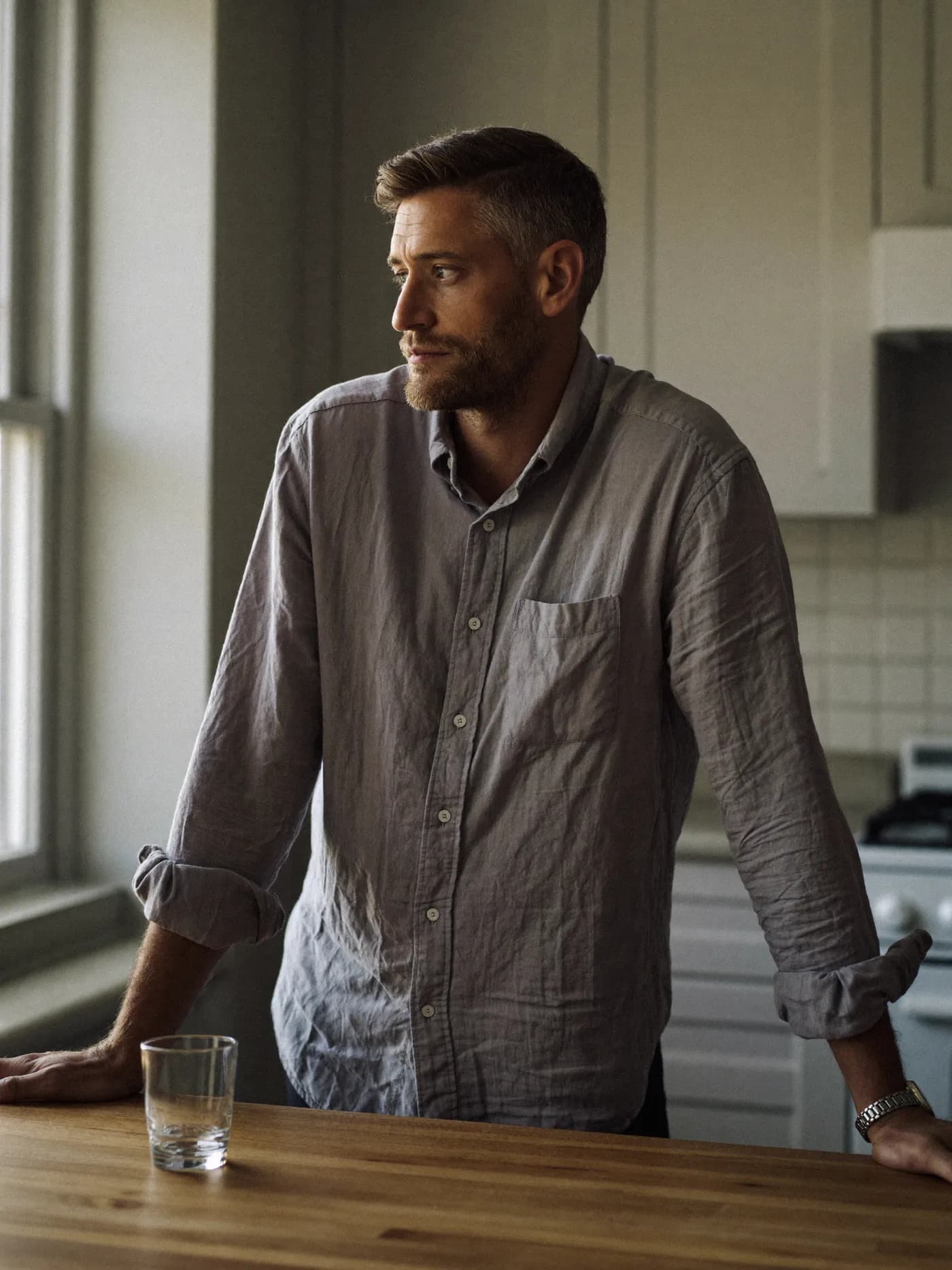 A man at his kitchen bench at dawn with a glass of water